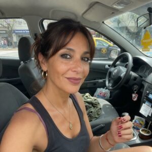 Mujer sonriente de cabello oscuro en el interior de un automóvil, tomando selfie con expresión alegre