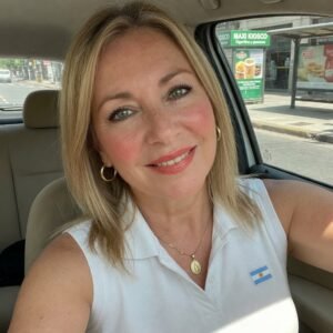 Retrato de una mujer rubia madura sonriente dentro de un automóvil, con cabello rubio y vestimenta casual.