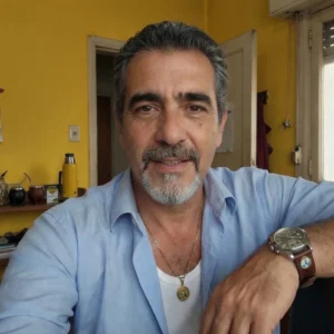 Retrato de un hombre maduro con cabello y barba entrecana, vestido con camisa celeste, en un ambiente cálido y cotidiano.