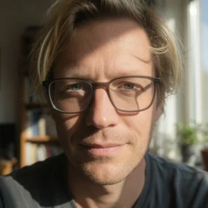 Retrato profesional de un hombre con anteojos y expresión cercana, iluminado por luz natural con estanterías de libros de fondo, representando el perfil de un abogado
