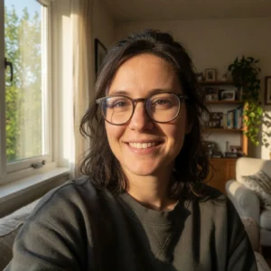 Mujer sonriente con anteojos en ambiente luminoso con luz natural, ventana y estantería de fondo