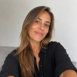 Retrato de una clienta del Estudio Sánchez Ferré sonriendo ante una pared blanca, con un sofá gris al fondo, tras pedir ayuda por la ocupación de su vivienda al terminar el contrato.